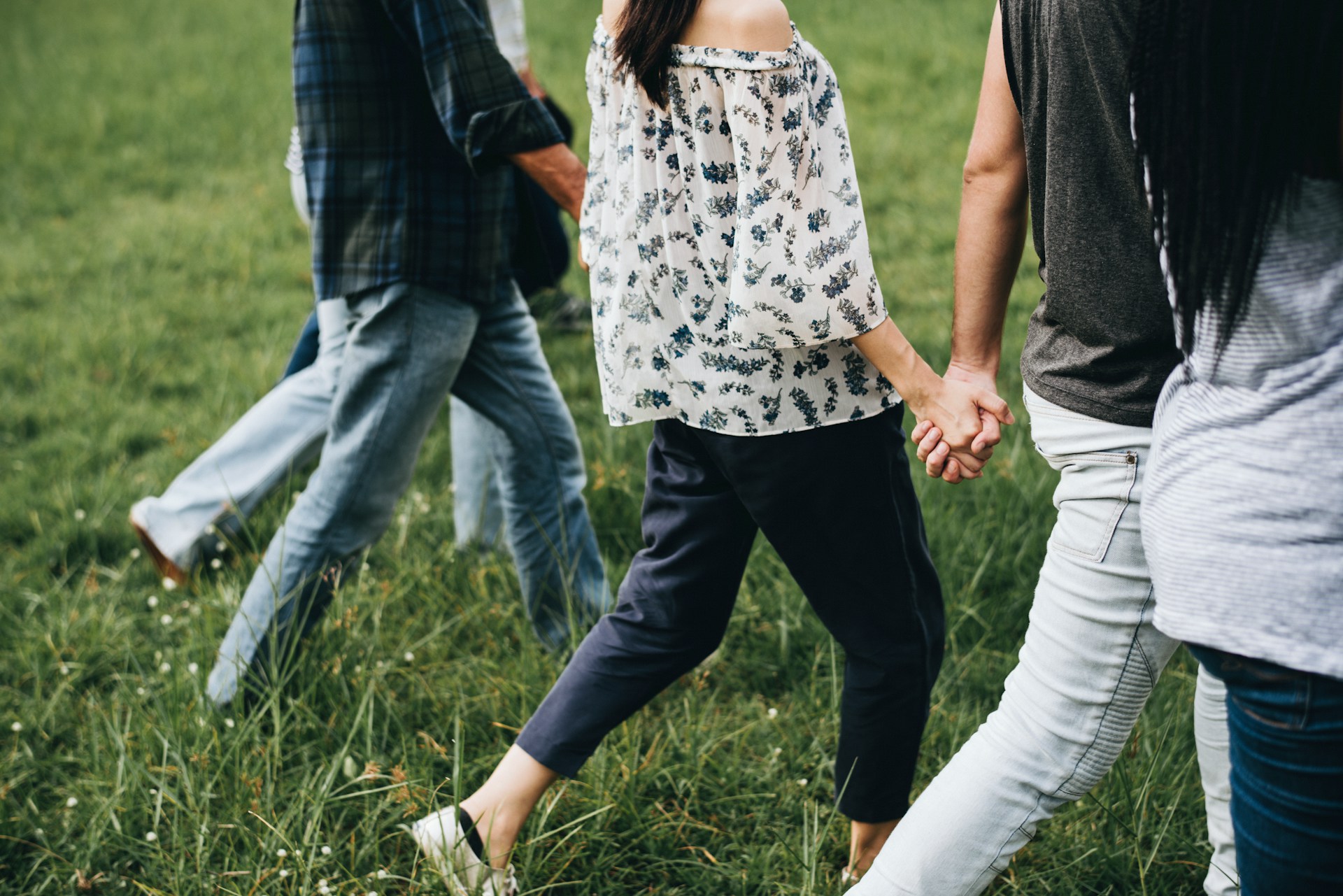 A blended family, shown from the shoulders down, hold hands while crossing a grassy field, representing blended families and trust disputes.
