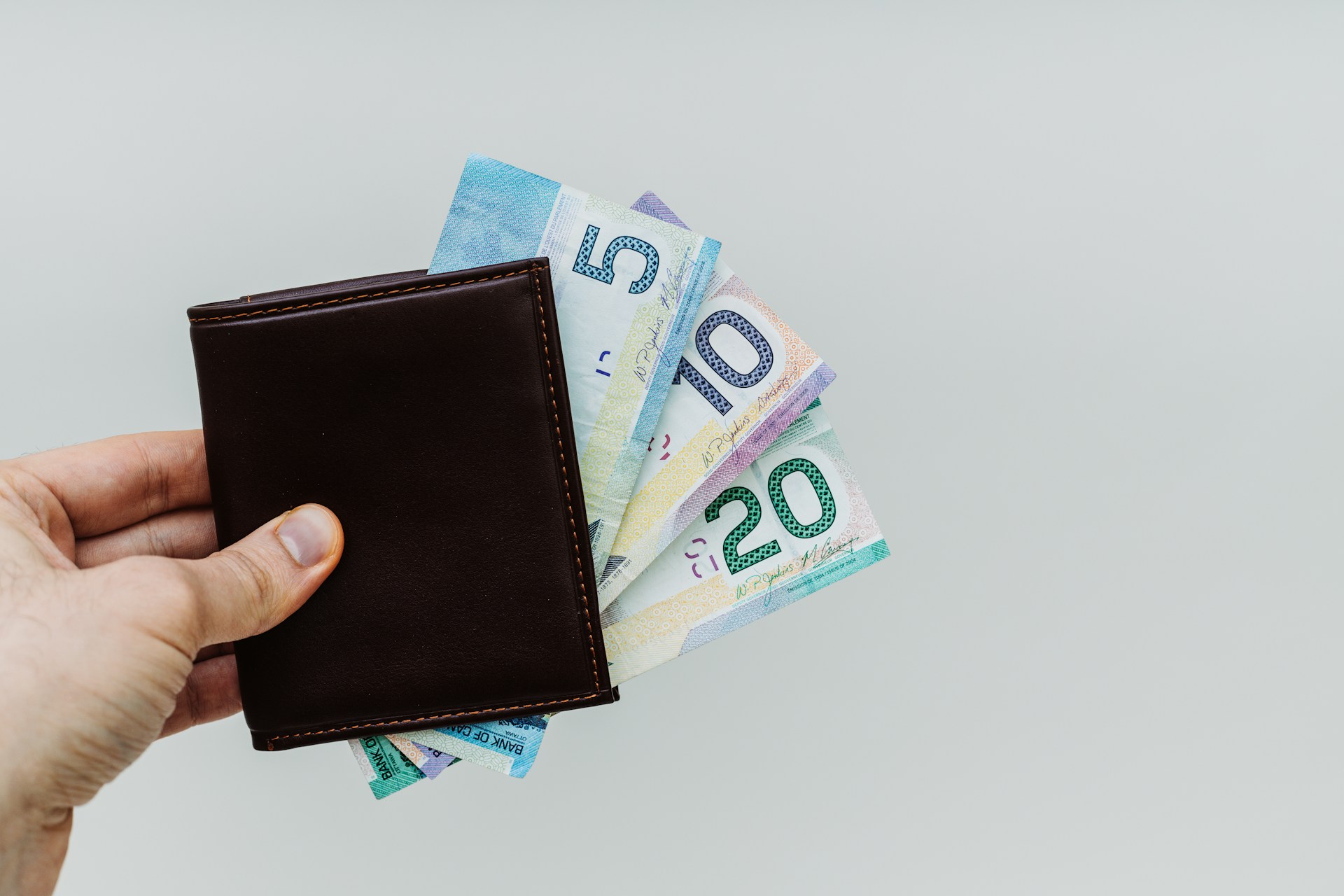 A brown leather wallet pinched between fingers with five, ten, and twenty dollar bills poking out and representing gift or loan estate disputes.
