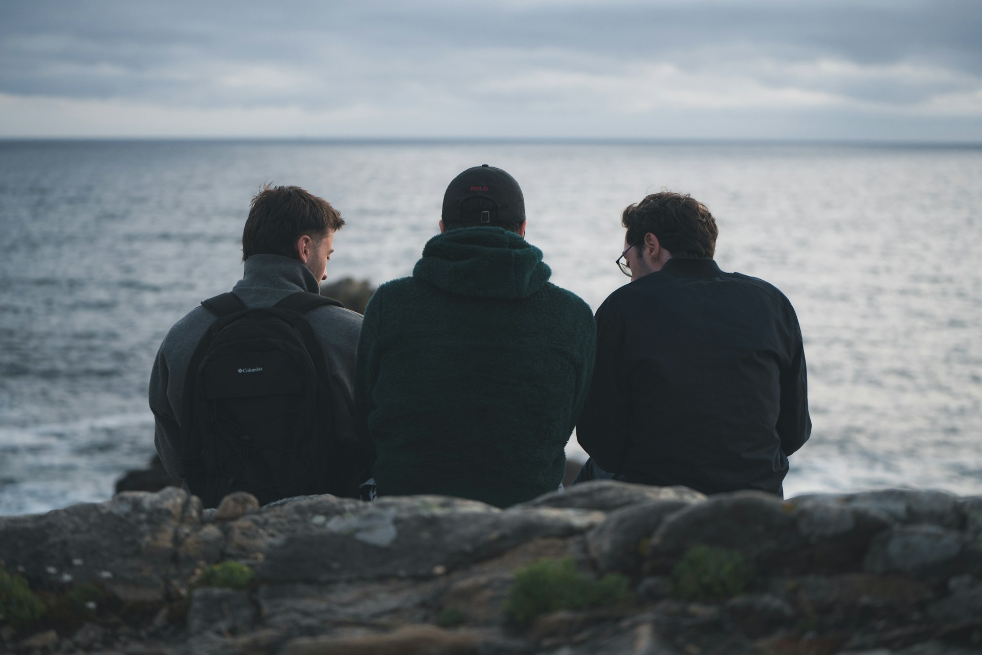 Three brothers sit on a rocky shoreline overlooking the sea under a overcast sky, representing drafting errors in wills.